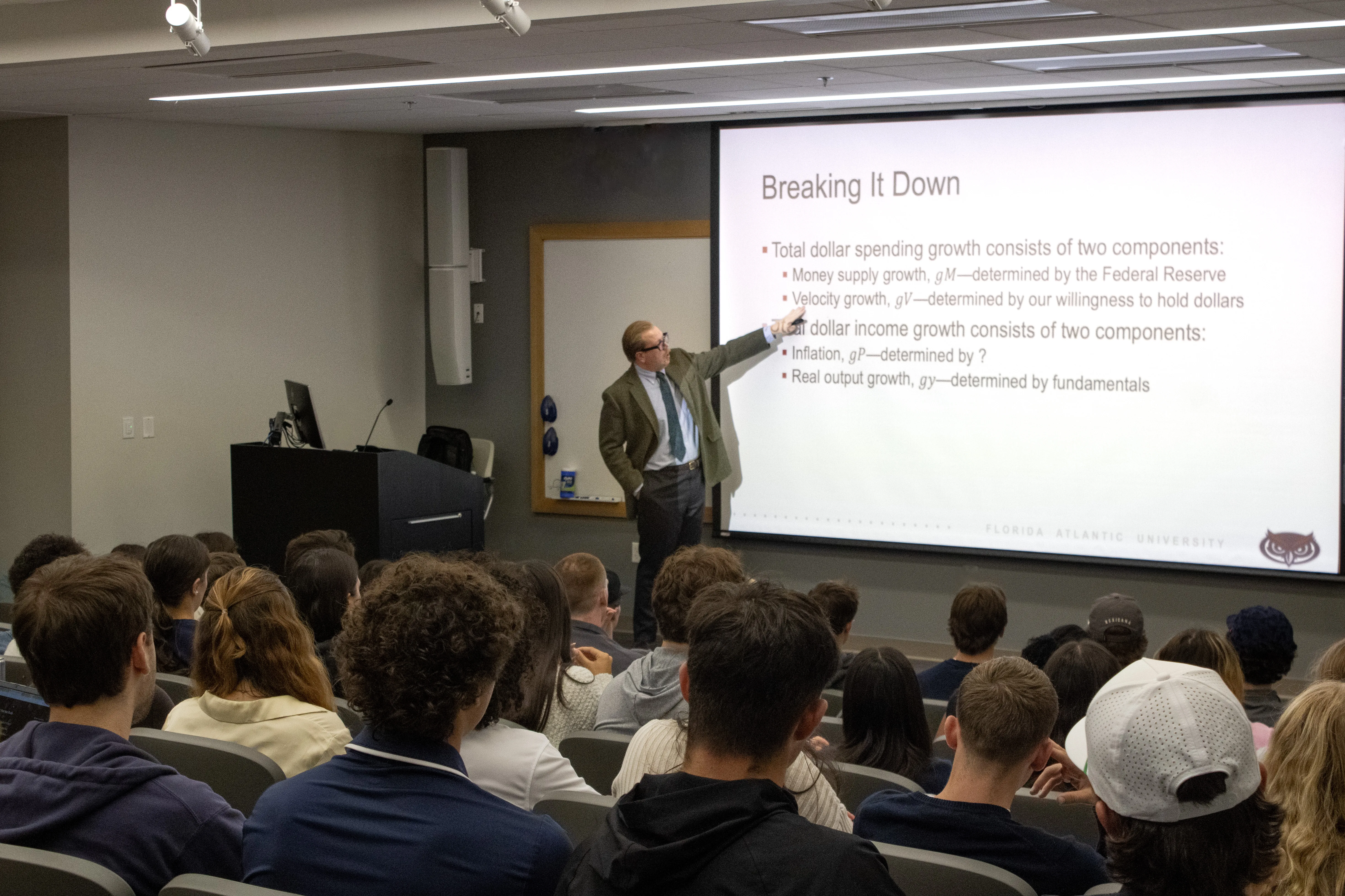 Bryan Cutsinger pointing to a slide while lecturing on inflation to a full lecture hall at Salve Regina University